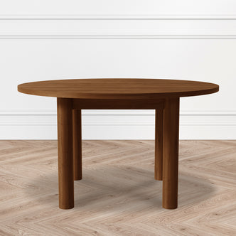 Hudson 80cm Round Hardwood Coffee Table in Walnut features a smooth, walnut-toned top with three sturdy cylindrical legs, set against a chevron-patterned wood floor and white paneled wall.