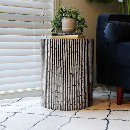 Ivo Mother of Pearl Inlay Side Table in Ivory & Black with a vertical strip mosaic pattern, topped with books and a plant, beside a dark blue sofa and light area rug.