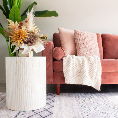 Ivo Mother of Pearl Inlay Side Table in Cream with striped mosaic detail, featuring a round surface, complements a rose-pink velvet sofa and cream throw in a cozy living-room setting.