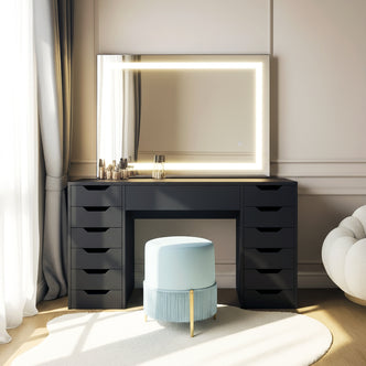 Janika Dressing Table with Storage & LED Lights in Black features a matte-black desk, frameless LED mirror, pale blue ottoman, and makeup items, all set in a modern, light-filled room.