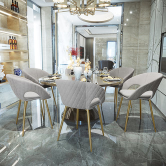 Jazlyn Fabric Dining Chairs with Gold Legs Set of 2 in Grey surround a round dining table, showcasing sleek upholstered seats on slender gold-toned legs, enhancing the contemporary dining space's elegance.