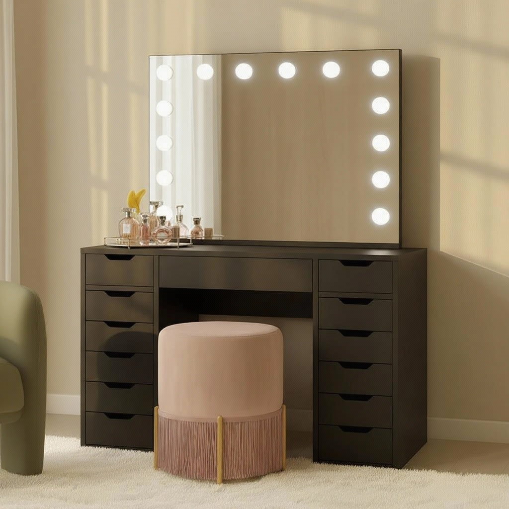 Jenna Hollywood Makeup Vanity Table with LED Mirror in Black features a black table, large mirror with LED lights, perfume bottles, and accessories, complemented by a pink stool with fringe on a light carpet.