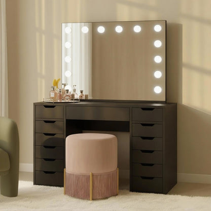 Jenna Hollywood Makeup Vanity Table with LED Mirror in Black features a black table, large mirror with LED lights, perfume bottles, and accessories, complemented by a pink stool with fringe on a light carpet.