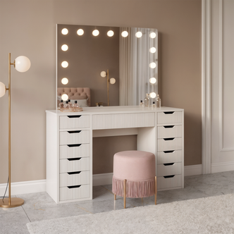 Jenna Fluted Makeup Vanity Table with Hollywood LED Mirror in White, featuring a large mirror with 13 bulbs, 13 drawers, and a spacious tabletop. Paired with a pink stool and gold lamp.