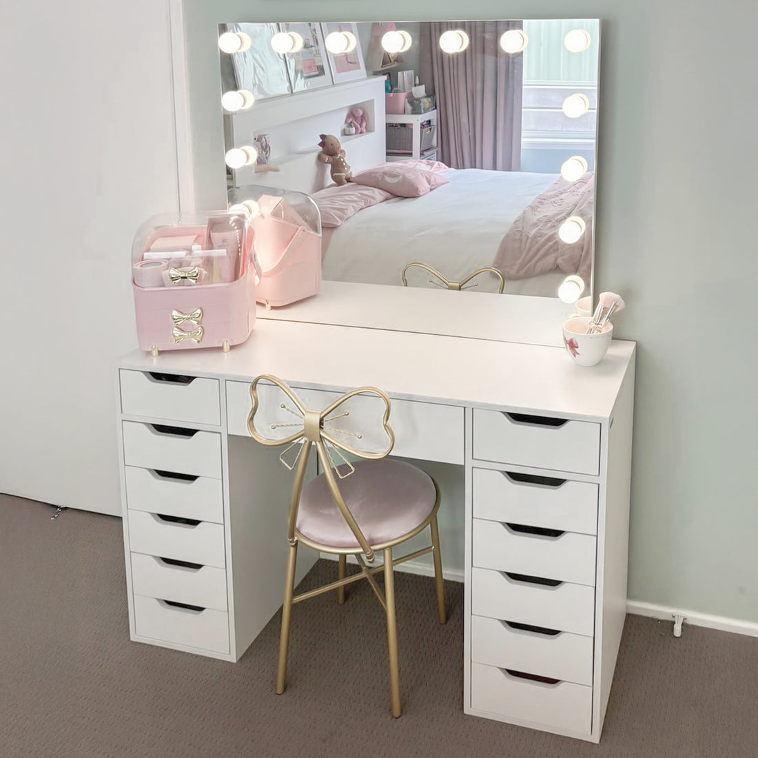 Jenna Hollywood Makeup Vanity Table with LED Mirror in White features a large lit mirror, 13 drawers, pink organizer, makeup brushes, and a gold chair with a bow backrest.