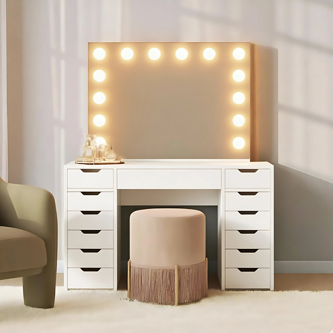 Jenna Hollywood Makeup Vanity Table with LED Mirror in White, featuring a white desk with stacked drawers, a large Hollywood-style mirror with bulbs, a tray with bottles, and a round stool.