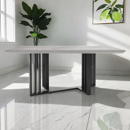 Joel 180cm 4-6 Seater Modern Dining Table in Concrete features a light-gray tabletop with a geometric black-metal base, set in a bright room with a marble-patterned floor and sunlight streaming in.