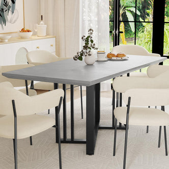 Joel 180cm 4-6 Seater Modern Dining Table in Concrete with sleek slate-gray top, black metal base, surrounded by six cream chairs; centerpiece of a bright dining area with a vase and tableware.