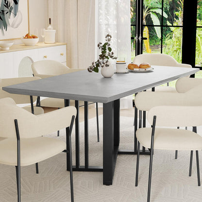 Joel 180cm 4-6 Seater Modern Dining Table in Concrete with sleek slate-gray top, black metal base, surrounded by six cream chairs; centerpiece of a bright dining area with a vase and tableware.