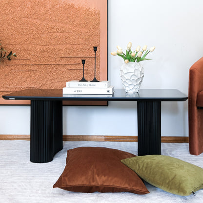 Joyce 120cm Coffee Table with Round Fluted Legs in Black, featuring a sleek finish and generous surface, styled with books, candlesticks, and a vase, set in a modern living room.