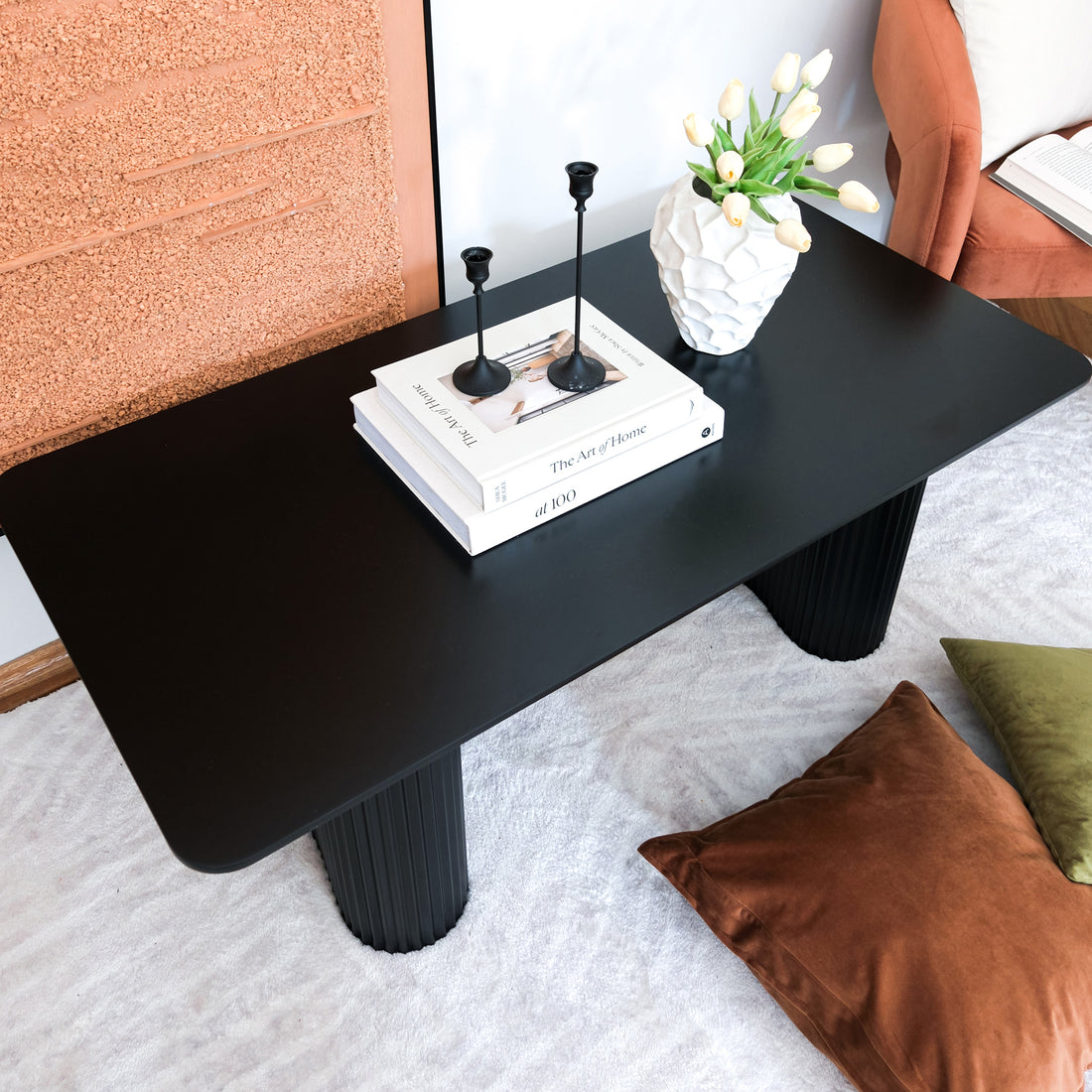 Joyce 120cm Coffee Table with Round Fluted Legs in Black, featuring a sleek design with stacked books, candleholders, and a faceted vase on a plush rug, enhancing modern living room aesthetics.