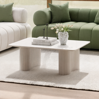 Joyce 120cm Coffee Table with Round Fluted Legs in White, featuring a smooth top, complements tufted sofas. Elegant centerpiece with books, candlesticks, and tulips, set on a plush rug.