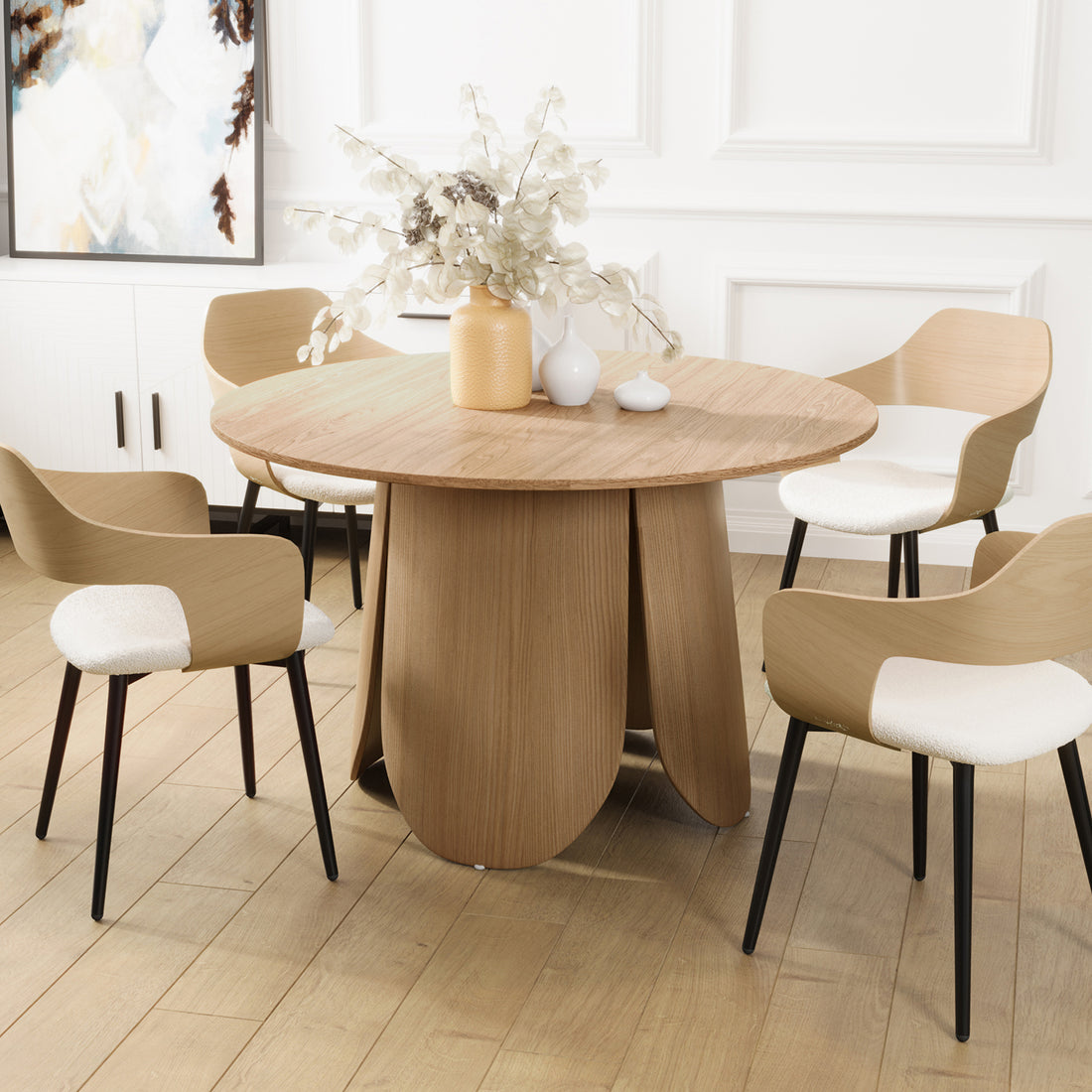 Kalyani 120cm Wooden Round Dining Table with Veneer Top Oak, featuring a sculptural petal-like base, surrounded by five light-wood chairs with white upholstered seats and slender black legs.