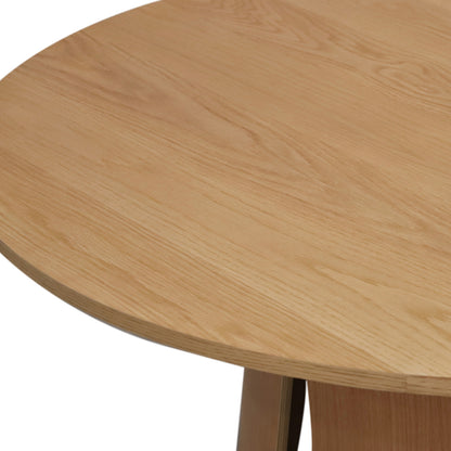 Kalyani 120cm Wooden Round Dining Table with Veneer Top Oak, showcasing a smooth tabletop with visible wood grain and a glimpse of its sturdy supporting leg structure beneath.