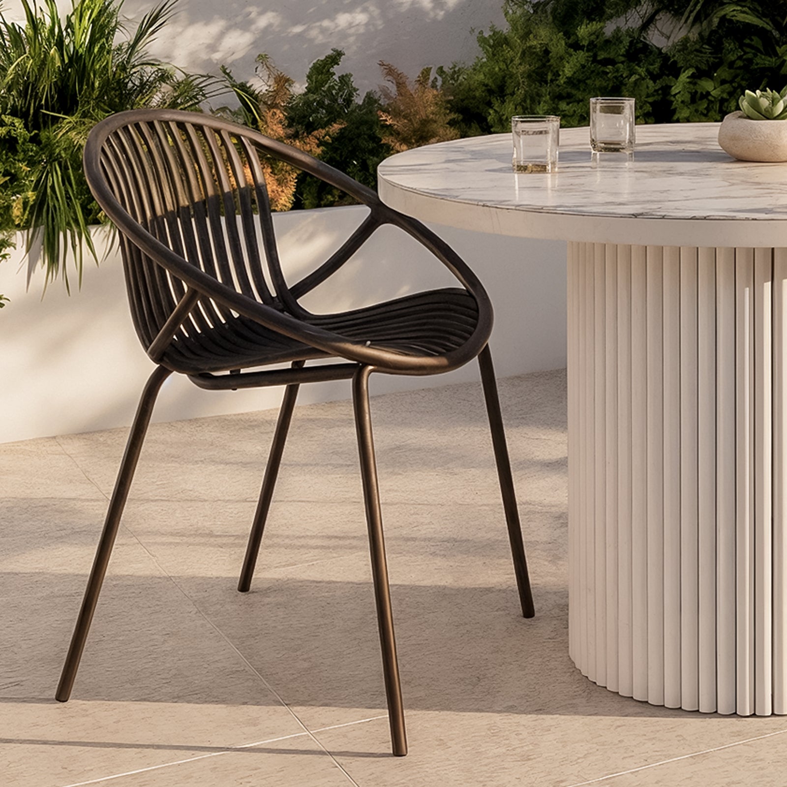Kosmos Outdoor Round Dining Chair Set of 2 in Black features a sleek wire design with powder-coated metal legs, positioned beside a round table with a marble-look top on a patio setting.