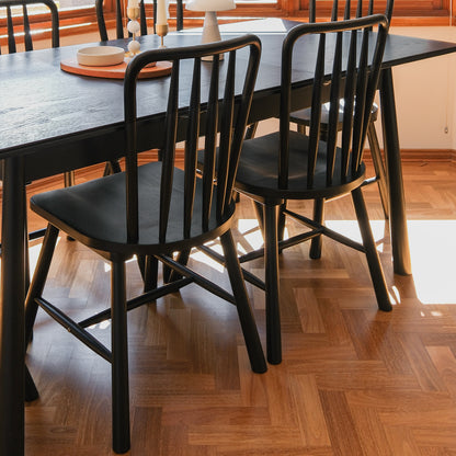 Leigh Solid Oak High-back Dining Chair Black Set of 2, shown in a dining-room corner with dark wood table, spindle-back design, and round tray with bowl and candlesticks, highlighting modern farmhouse style.
