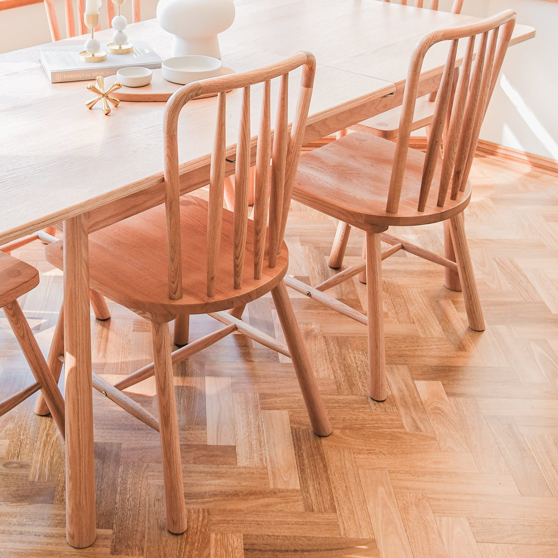 Leigh Solid Oak High-back Dining Chair Natural Set of 2 around a light-wood table in a minimalist dining area, showcasing spindle-back design and a chevron-patterned floor with chic tabletop decor.