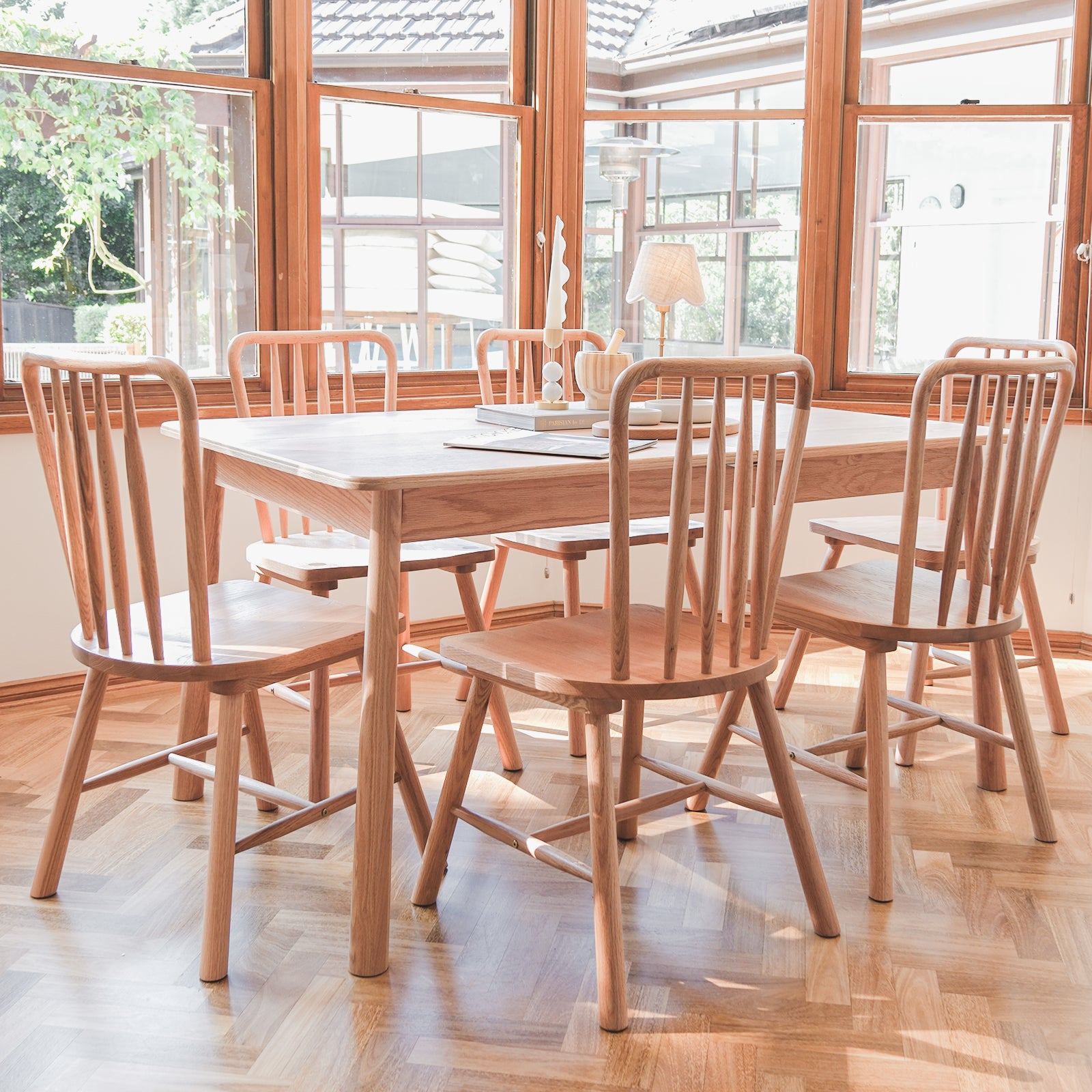 Leigh Solid Oak High-back Dining Chair Natural Set of 2 in a sunlit dining nook with spindle-back design, showcasing the chairs' elegant, tall backs and solid wood build against a herringbone parquet floor.