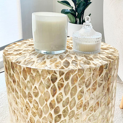 Lulu Mother of Pearl Inlay Side Table in Sand features a teardrop mosaic design with creamy tones, topped with white candles in glass vessels and a small green plant, enhancing its elegance.