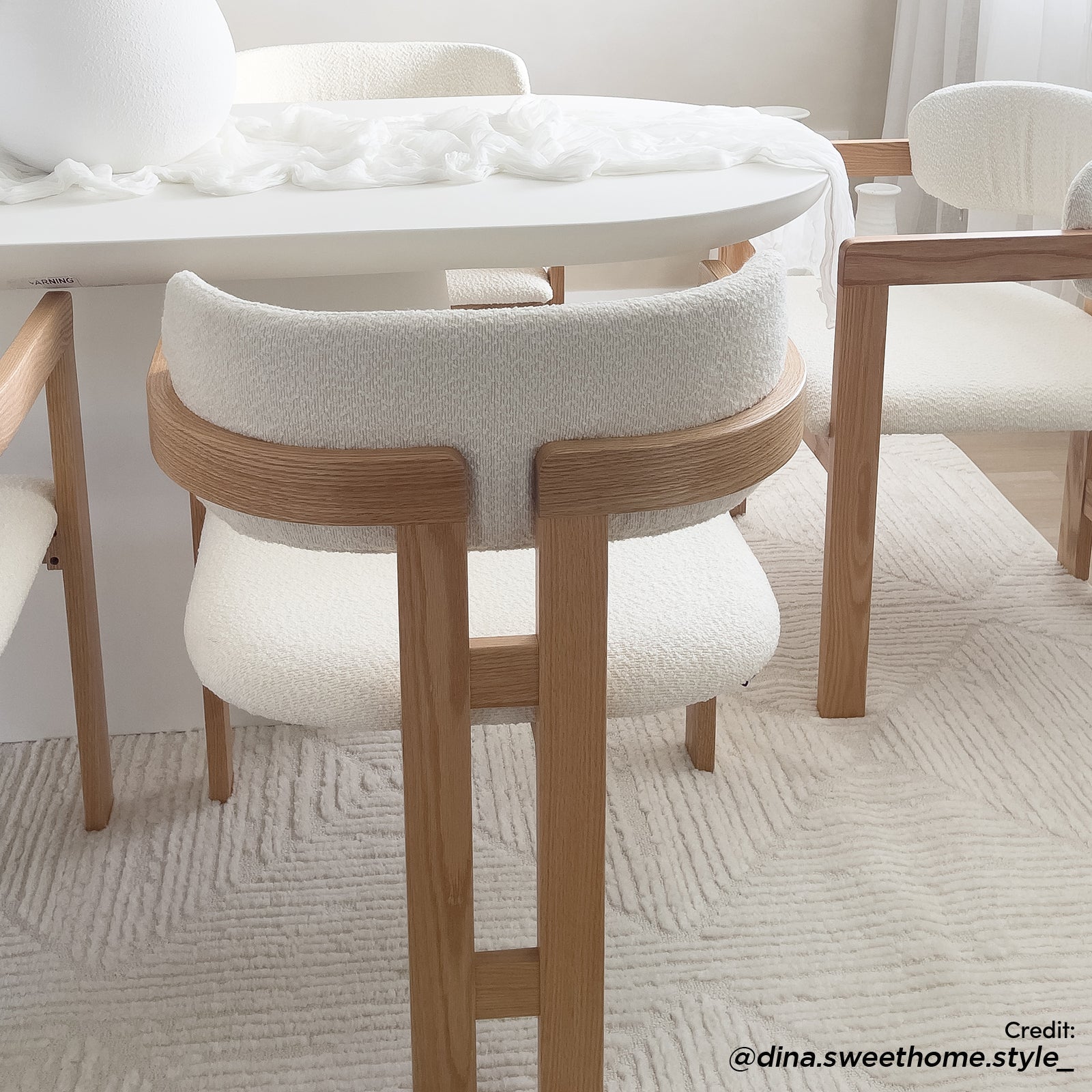 Maddi Boucle Hardwood Dining Chair in Cream White: Modern design with pale oak frame, curved back, and textured off-white boucle upholstery, set in a minimalist dining nook with matching furniture and soft decor elements.