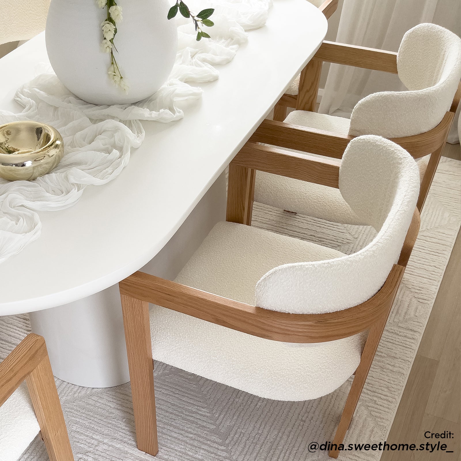 Maddi Boucle Hardwood Dining Chair in Cream White, featuring a curved backrest and upholstered in light boucle fabric, framed by warm wood, set around a modern white oval dining table.