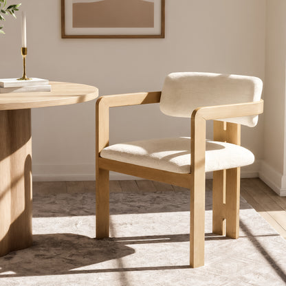 Maddi Boucle Hardwood Dining Chair in Cream White, featuring a light-wood frame with a curved backrest, upholstered in soft boucle fabric, placed beside a round wooden table in a minimalist setting.
