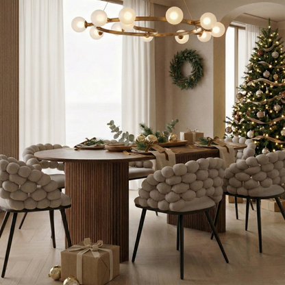 Marciana 8 Seater Fluted Oval Dining Table set for a festive meal with gold-tone flatware and pine centerpieces, surrounded by sculptural chairs, under a modern brass chandelier, beside a decorated Christmas tree.