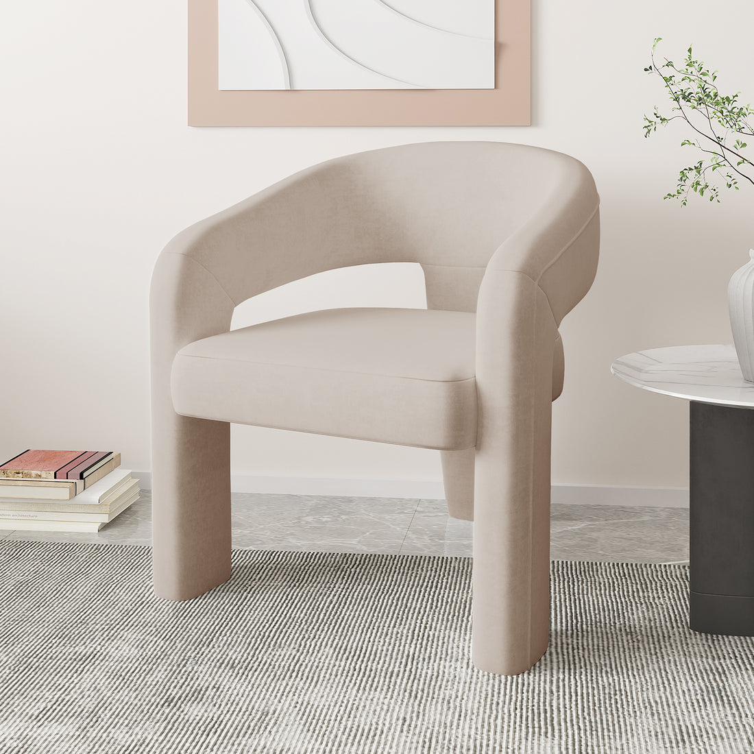 Mariah Velvet Upholstered Accent Chair - Beige, featuring a curved backrest with an open cut-out, rounded armrests, and tubular legs, placed on a striped rug with a side table nearby.