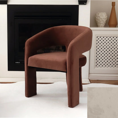 Mariah 3 Legged Velvet Accent Chair in Mocha Mousse with a curved backrest and armrests, positioned by a black-trimmed fireplace, on a light rug, next to decorative vases.