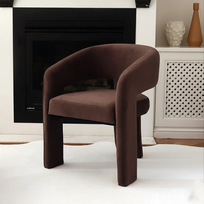 Mariah 3 Legged Velvet Accent Chair in Mocha Brown, showcased on a white rug before a black-trimmed fireplace, next to a white lattice cabinet adorned with two decorative vases.