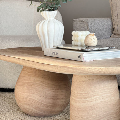 Mason 100cm Pillar Concrete Coffee Table in Beige with a sculptural vase, eucalyptus sprigs, AD at 100 book, marble tray, bubble candle, and stone match vessel atop, exuding minimalist elegance.