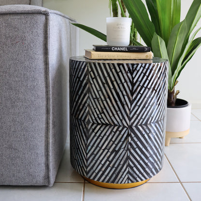 Merry 35cm Mother of Pearl Inlay Side Table in Ivory & Black beside a gray sofa, adorned with books and a candle, showcasing its elegant herringbone-style mosaic pattern.