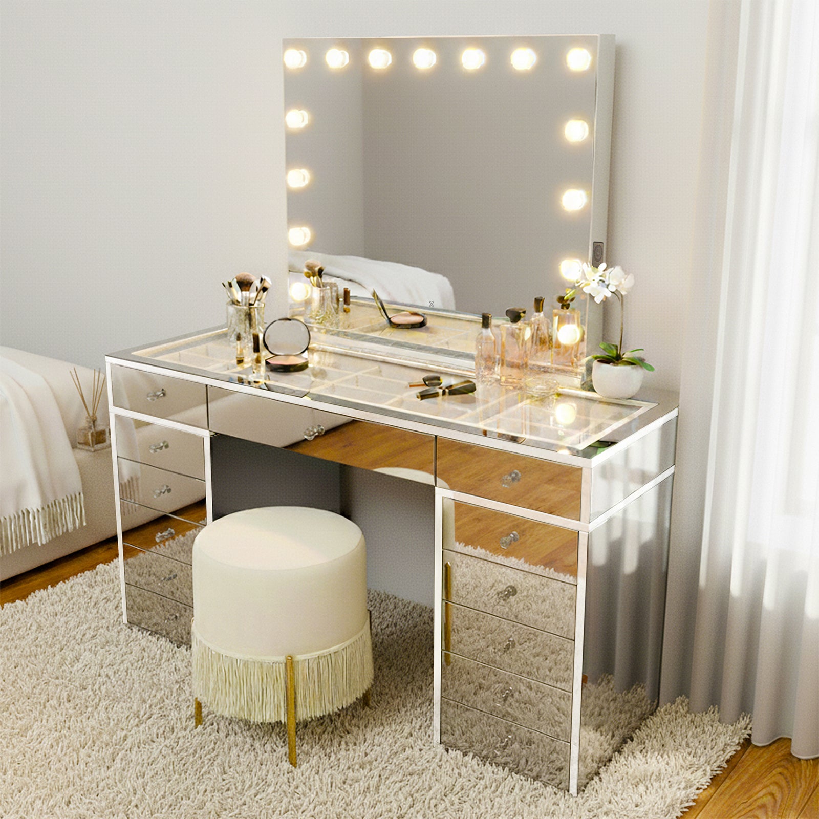 Monroe 13 Drawer Mirror Finish Hollywood LED Dressing Table with a large LED bulb mirror, mirrored drawers, crystal knobs, and a glass top, complemented by a round ivory stool and potted orchid.