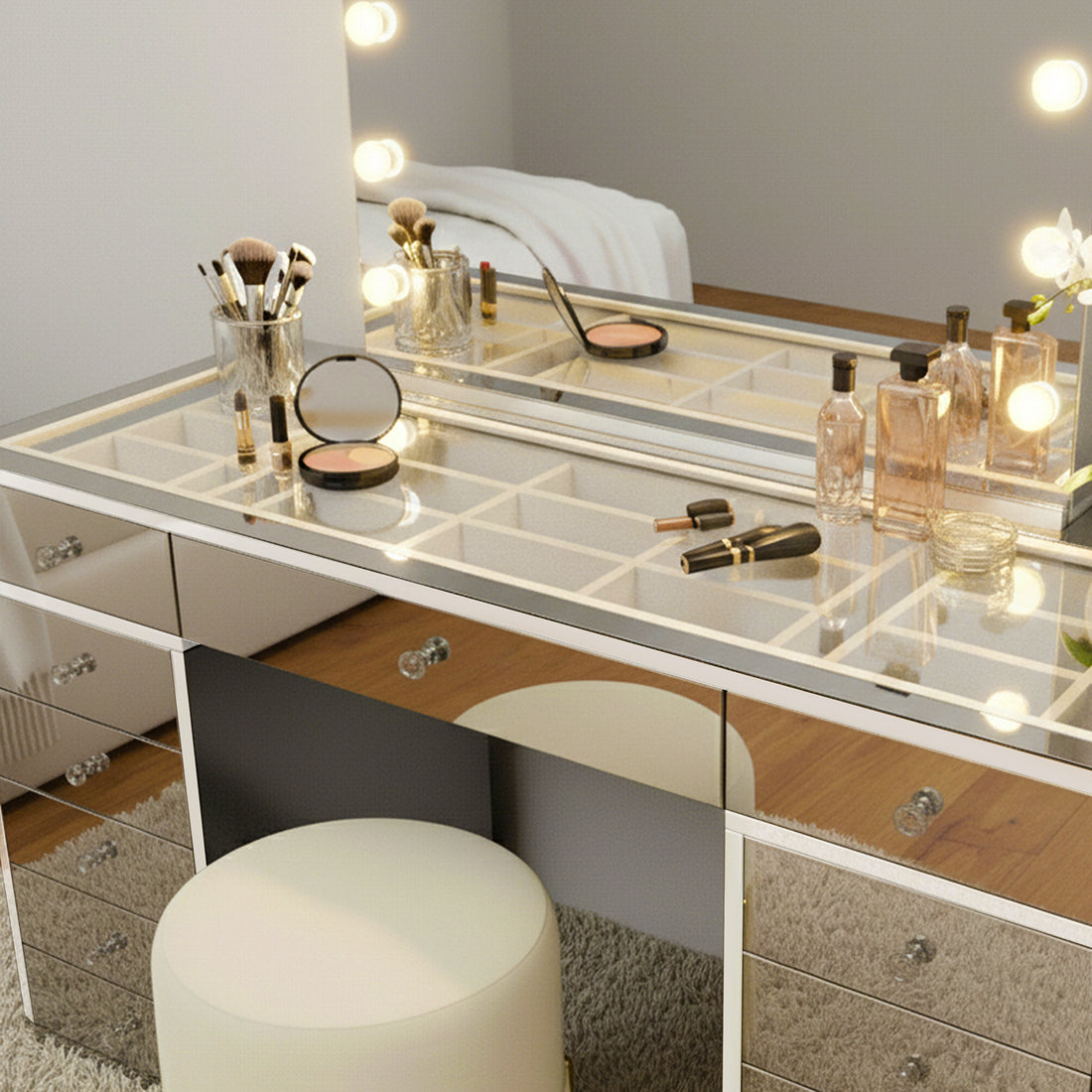 Monroe Hollywood Makeup Dressing Table in Silver with a lighted mirror, organized cosmetics, and a round stool. Features mirrored design, glass top, and compartmentalized storage on a soft rug.