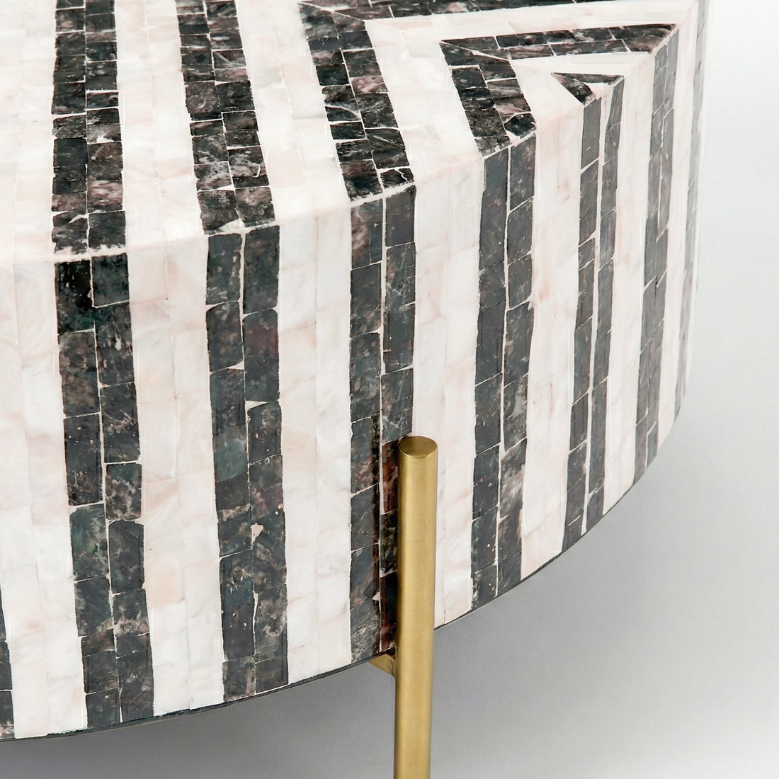 Close-up of edge and side of a mosaic patterned round table with gold leg on white background