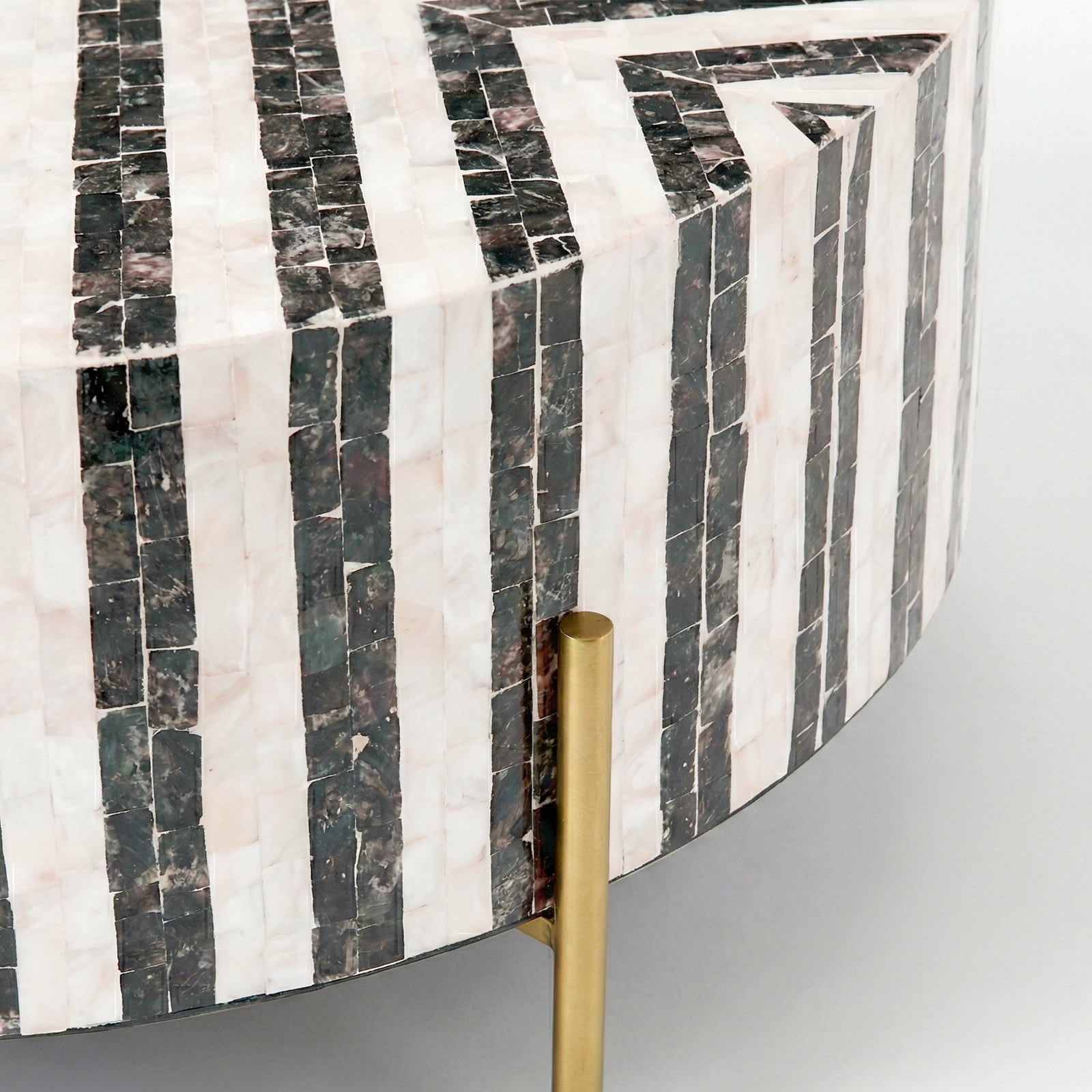 Close-up of edge and side of a mosaic patterned round table with gold leg on white background