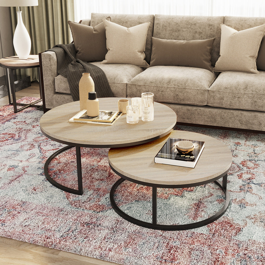 Nevada Round Nesting Coffee Table Set in Natural, featuring two round tables with light-wood tops and slender black-metal legs, styled with decorative items like a vase and books, set on a patterned rug.