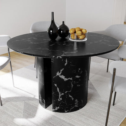 Nydia 120cm Round Dining Table - Black with a black-marble tabletop and cylindrical base, surrounded by light-gray upholstered chairs, styled with black vases and a bowl of lemons on a neutral rug.