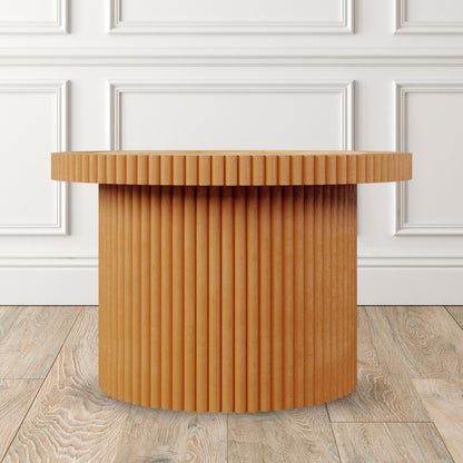 Nylah Natural Rattan Centre Coffee Table in Honey, drum-shaped with light-stained wood and vertical fluting, set against a white paneled wall.