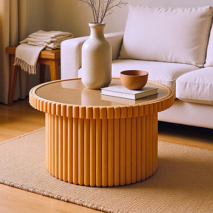 Nylah Natural Rattan Centre Coffee Table in Honey with a round glass top and fluted wooden base, adorned with a ceramic vase, terracotta bowl, and book, set on a jute rug.