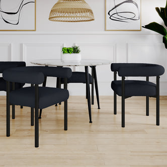 Ohio Curved Boucle Dining Chair Set of 2 in Black features low-backed, deep charcoal fabric, tubular metal legs, and curved backrests around a sleek marble-top table, enhancing a modern dining nook.