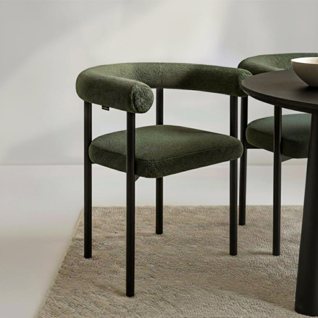 Ohio Curved Bouclé Dining Chair Set of 2 in Green features a sleek black metal frame and deep olive-green bouclé upholstery, visible in a modern dining-room vignette with a matching chair partially shown.