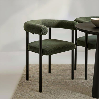 Ohio Curved Bouclé Dining Chair Set of 2 in Green features a sleek black metal frame and deep olive-green bouclé upholstery, visible in a modern dining-room vignette with a matching chair partially shown.