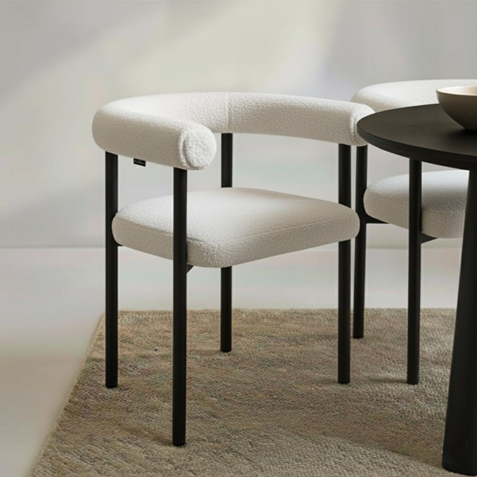 Ohio Curved Bouclé Dining Chair Set of 2 in Cream, featuring a rounded backrest and cushioned seat in off-white bouclé, with sleek black metal legs, arranged on a natural-fiber rug.