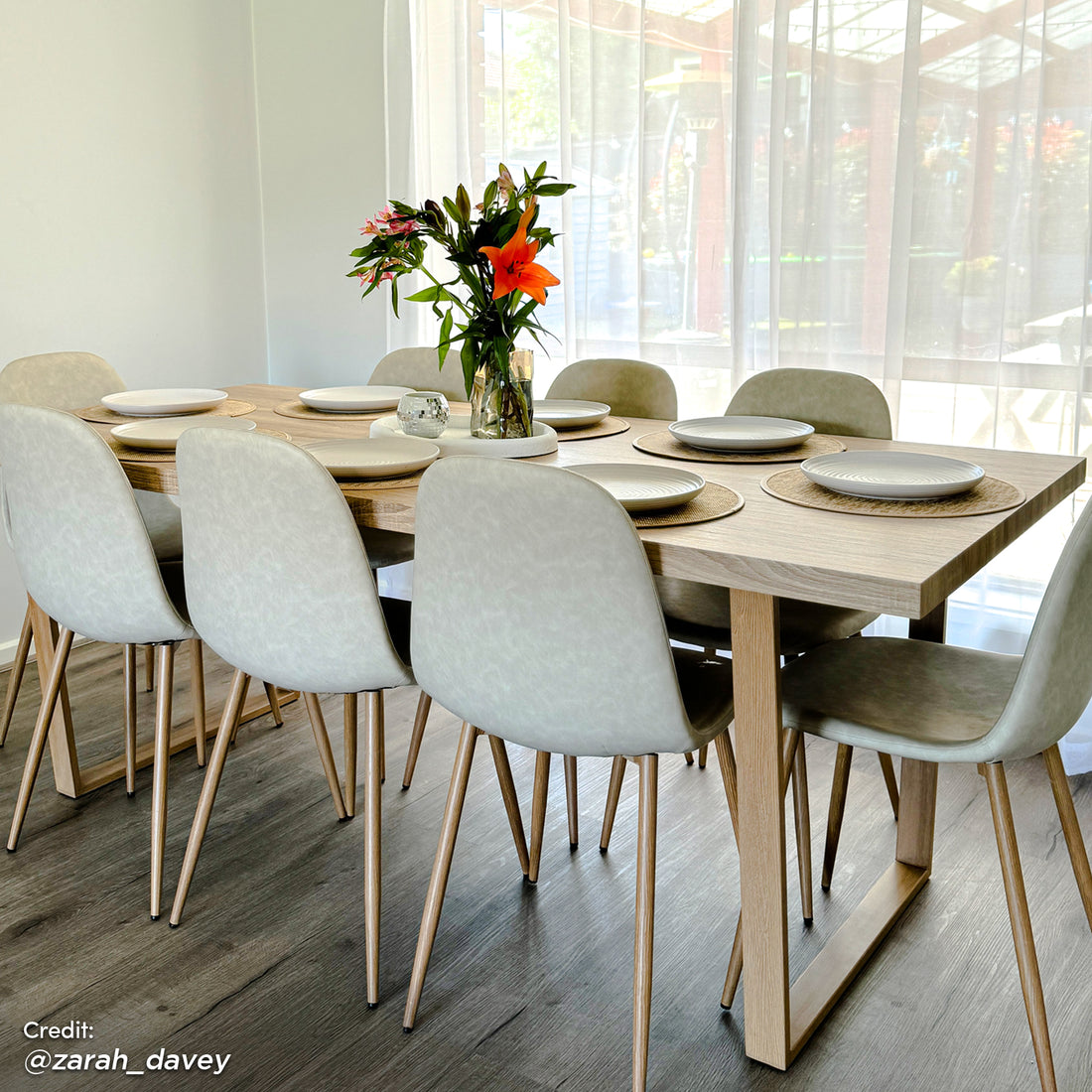 Oregon 200cm Industrial Dining Table - Natural featured in a minimalist setting with eight molded-shell chairs, woven placemats, white plates, and a glass vase with a floral bouquet, highlighting its elegant natural wood appearance.