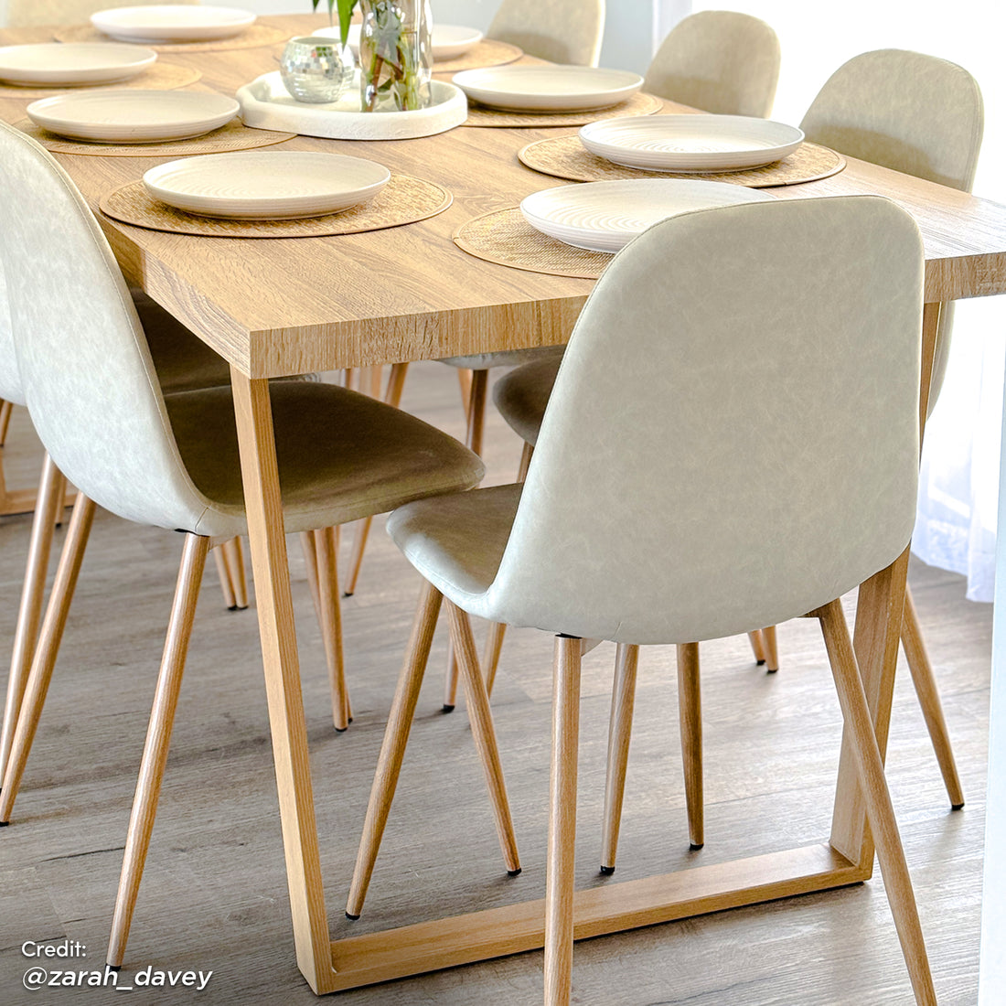 Oregon 200cm Industrial Dining Table - Natural, showcased with six cream faux-leather chairs, round woven placemats, and a greenery centerpiece, on a light wood floor in a bright room.