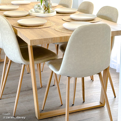 Oregon 200cm Industrial Dining Table - Natural, showcased with six cream faux-leather chairs, round woven placemats, and a greenery centerpiece, on a light wood floor in a bright room.