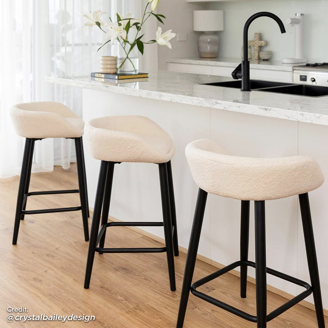 Peyton Bouclé Bar Stool Set of 2 in Cream features soft bouclé upholstery and slim black metal legs with footrests, elegantly placed by a modern kitchen island with marble top.