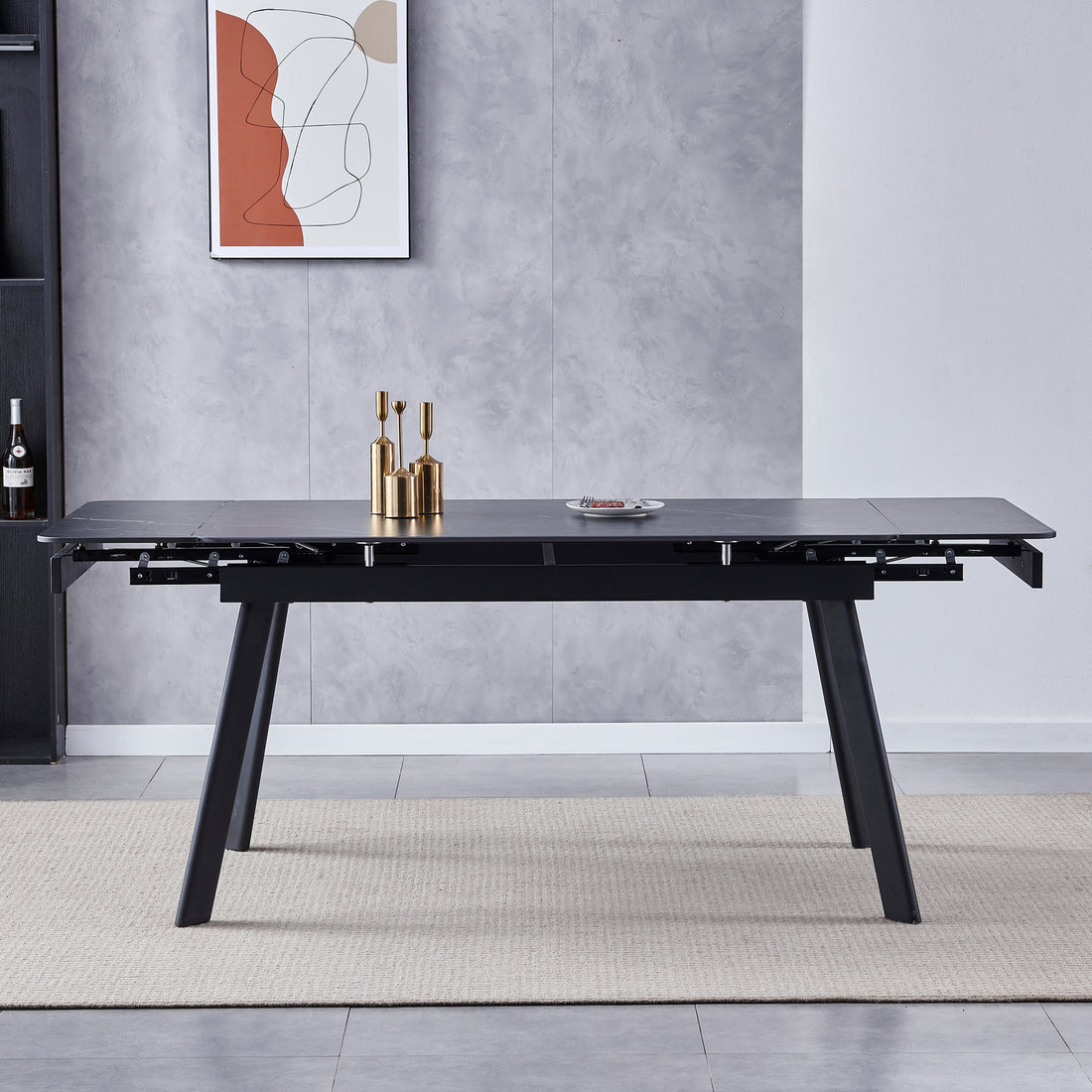 Rheed 197cm Extendable Ceramic Dining Table in Black with matte top and splayed legs, featuring a metal extension mechanism, brass vases, white plate with berries, and a neutral-tone rug underneath.