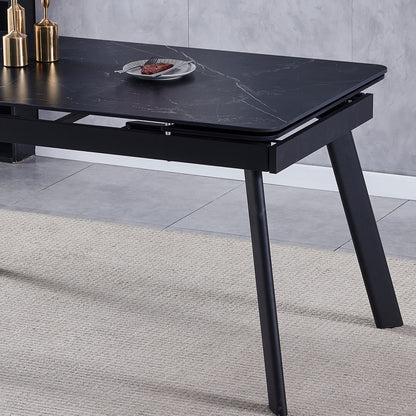 Rheed 197cm Extendable Ceramic Dining Table in Black with a faux-marble finish, splayed metal legs, and adorned with brass decorative vessels. A slice of meat and fork rest on a plate.